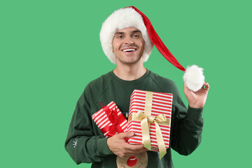 Sticker - Happy young man in Santa hat with gift boxes on green background