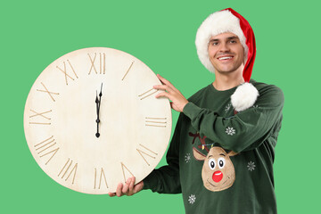 Sticker - Happy young man in Santa hat with big clock on green background. Christmas countdown concept