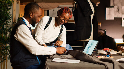 Wall Mural - Tailor and assistant picking fabric to create modern clothes, working in atelier to craft clothing items for fashion collection. Two designers choosing material, handmade. Handheld shot.