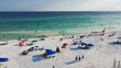 Colorful tents, beach lounge chairs, canopy and crowded of people swimming, relaxing, walking along white sandy shoreline with turquoise water, South Walton beach, Destin, Florida