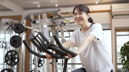 Wall Mural - スポーツジムでエアロバイクに乗る女性