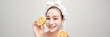 Young woman applying clay mask on her mask with sliced fruit in hand over color banner