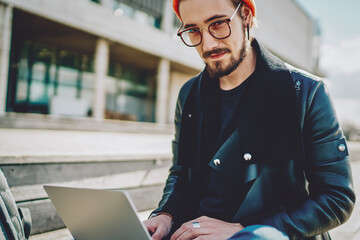 Wall Mural - Portrait of skilled man dressed in stylish outfit sitting outdoors with modern netbook