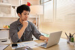 © Puwasit Inyavileart - Handsome young man sits working at a desk with a laptop and office equipment, Smiling young man ready for work at the start of the week. Positive Start to a Productive Workweek.