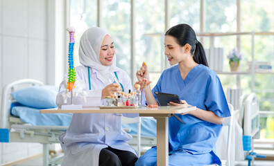 Wall Mural - Asian professional successful experienced muslim female doctor in white lab coat with hijab stethoscope discussing brainstorming advising assistant nurse in blue uniform about medicines in hospital