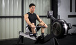 © chadchai - Fitness-conscious man passionately engaging in indoor rowing, in well-equipped gym