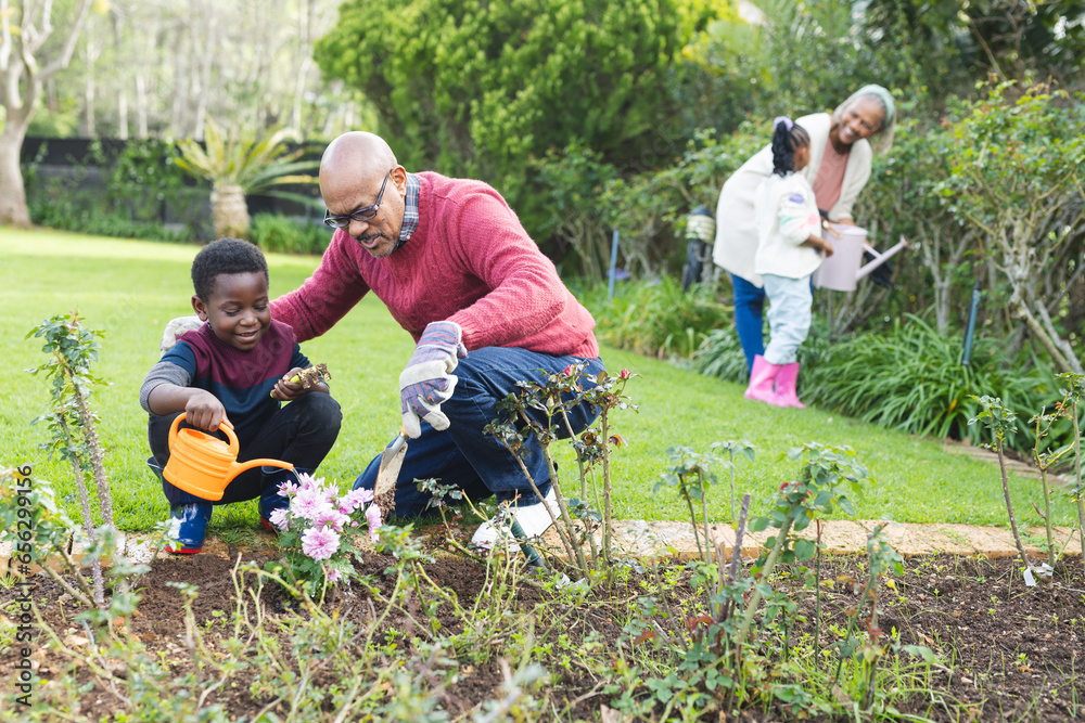 Happy african american grandparents and grandchildren watering plants ...