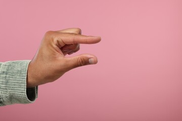 Man holding something in hand on pink background, closeup. Space for text