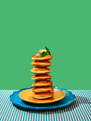 Wall Mural - Food pop art photography. Delicious sweet pancakes with maple syrup and batter on plates over green background. Vintage, retro 80s, 70s style. Complementary colors.