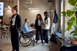 © Maskot - Female colleagues discussing with disabled businessman at creative office