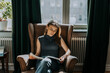 © Maskot - Teenage girl reading book while sitting on armchair against window at library