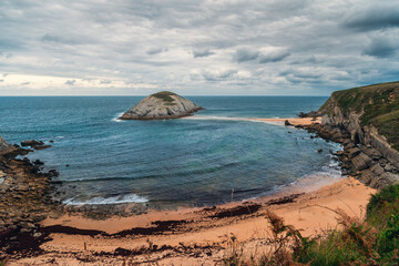 Wall Mural - Playa de Covachos beach in Santander, Cantabria, North Spain with rocky island and sandy spit in cloudy day. Popular travel destination