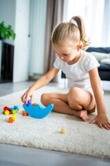 Wall Mural - Little girl playing with wooden balancing toy on the floor in home living room. 