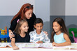 © Chiralli - Teacher and school student children studying at desk in educational classroom, writing in notebook, reading book. Group of diverse classmates learning. Academic Concept.