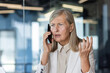 © Liubomir - Close-up photo. Worried and upset senior business woman talking on the phone in the office and spreading her hands.
