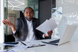 © Liubomir - Portrait of a worried African-American man holding documents, papers, agreements in his hands. Sitting in the office at the desk and throwing his arms at the camera in frustration.