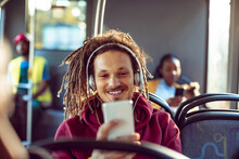 Young mixed man listening to music on his smartphone while riding on the bus