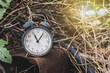 The concept of waiting and wasted time. An old battered and rusty black alarm clock vintage retro style that was abandoned with old materials in a wasteland full of weeds.