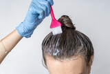 Close-up of a woman's heClose-up of a woman's head in the process of hair coloring on a white background. Closeup woman hands dyeing hair using a brush. Colouring of white hair at home.