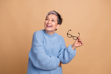 Sticker - Portrait of smart cheerful lady hold eyeglasses look empty space brainstorming isolated on beige color background