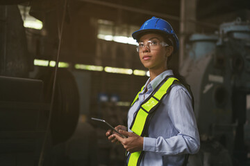 Wall Mural - Female engineer worker working with digital tablet at the industry factory area. Female technician wear safety helmet, glasses and uniform checking and working in the factory