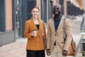 Poster - Two young successful brokers in quiet luxury apparel looking at camera with smiles while one of them holding cup of takeaway coffee