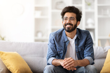 Wall Mural - Smiling Young Eastern Guy Relaxing On Couch In Living Room At Home