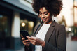 © Jasmina - Beautiful black professional woman scrolling on her phone on the street