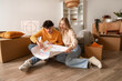 © Pixel-Shot - Young couple with house plan sitting in room on moving day