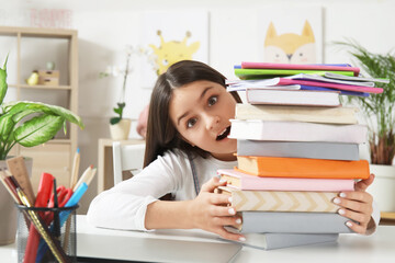 Wall Mural - Surprised little girl with stack of schoolbooks at home