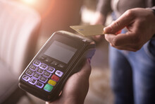 NFC credit card payment. Woman paying with contactless credit card with NFC technology. Wireless money transaction. Card machine in male hand on sunlight background