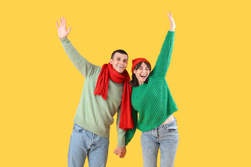 Beautiful young couple in warm clothes on yellow background