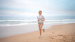 Woman jogging on beach. Sporty female jogging on sand beach, waves on background. Full body view woman in mini shorts and t-shirt who runs alongside ocean. Outdoor workout of trained fit girl. 