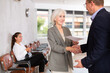 © JackF - Positive mature female legal adviser has signed successful contract and shakes hands with middle-aged male client. In office, visitors waiting for invitation to lawyer in background