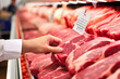 Close up of person hand comparing beef prices at the supermarket, choosing the right piece of meat at the shop