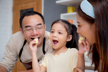 Wall Mural - Happy family with father, mother and daughter in kitchen while daughter feed apple fruit together at home, happiness mom, dad and child with bonding and relation, lifestyles and nutrition concept.