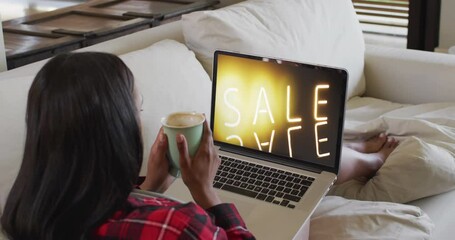 Sticker - Biracial woman on couch with coffee, using laptop for online shopping, slow motion