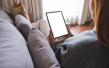 Mockup image of a woman holding digital tablet with blank desktop screen while lying on a sofa at home