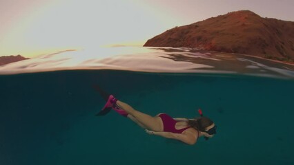 Canvas Print - Cinemagraph of the woman swimming underwater in the tropical sea at sunset. Frozen frame of the sea surface and moving underwater model