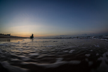 Wall Mural - Silhouettes of fishermen on the beach pushing wooden boats out to sea to fish wooden boats on Ho Coc Vung Tau beach