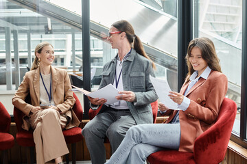 three cheerful team members sitting on red chairs and discussing paperwork, coworking concept