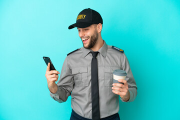 Wall Mural - Young security man isolated on blue background holding coffee to take away and a mobile