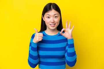 Poster - Young Chinese woman isolated on yellow background showing ok sign and thumb up gesture