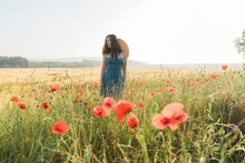 Woman With Hat Standing Amidst Red Poppy Flowers In Field