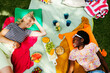 © Westend61 - Smiling friends lying on picnic blanket in garden
