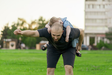 Wall Mural - young father holding her daughter on his back in the shape of plane, having fun outdoors