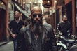 Handsome, bald, well-groomed bearded biker gangster in dark sunglasses, a vest, jacket, and tie against the backdrop of the street and motorcycles