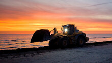 Bulldozer On The Beach At Sunset. A Large Tractor Cleans The Beach Of Sea Grass. Bulldozer In Motion And Blur.