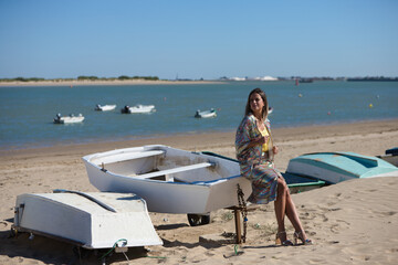 Pretty young blonde woman sitting in the fishermen's boats on the seashore. In the background on the horizon the blue sea and the biosphere reserve of the natural park and the mouth of the river