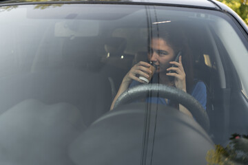 Wall Mural - Multitasking driver business lady driving a car drinking coffee and talking on a cell phone.